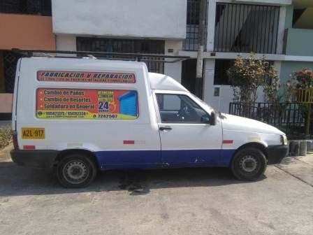 Una furgoneta de reparto blanca y azul aparcada en una calle junto a un edificio, con un colorido letrero en el lateral.