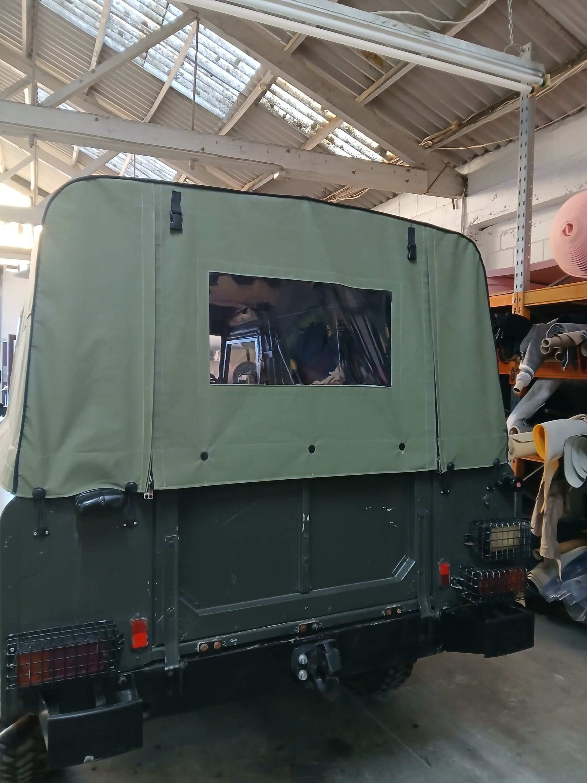 Green canvas truck cover with a rear window on a dark green vehicle.