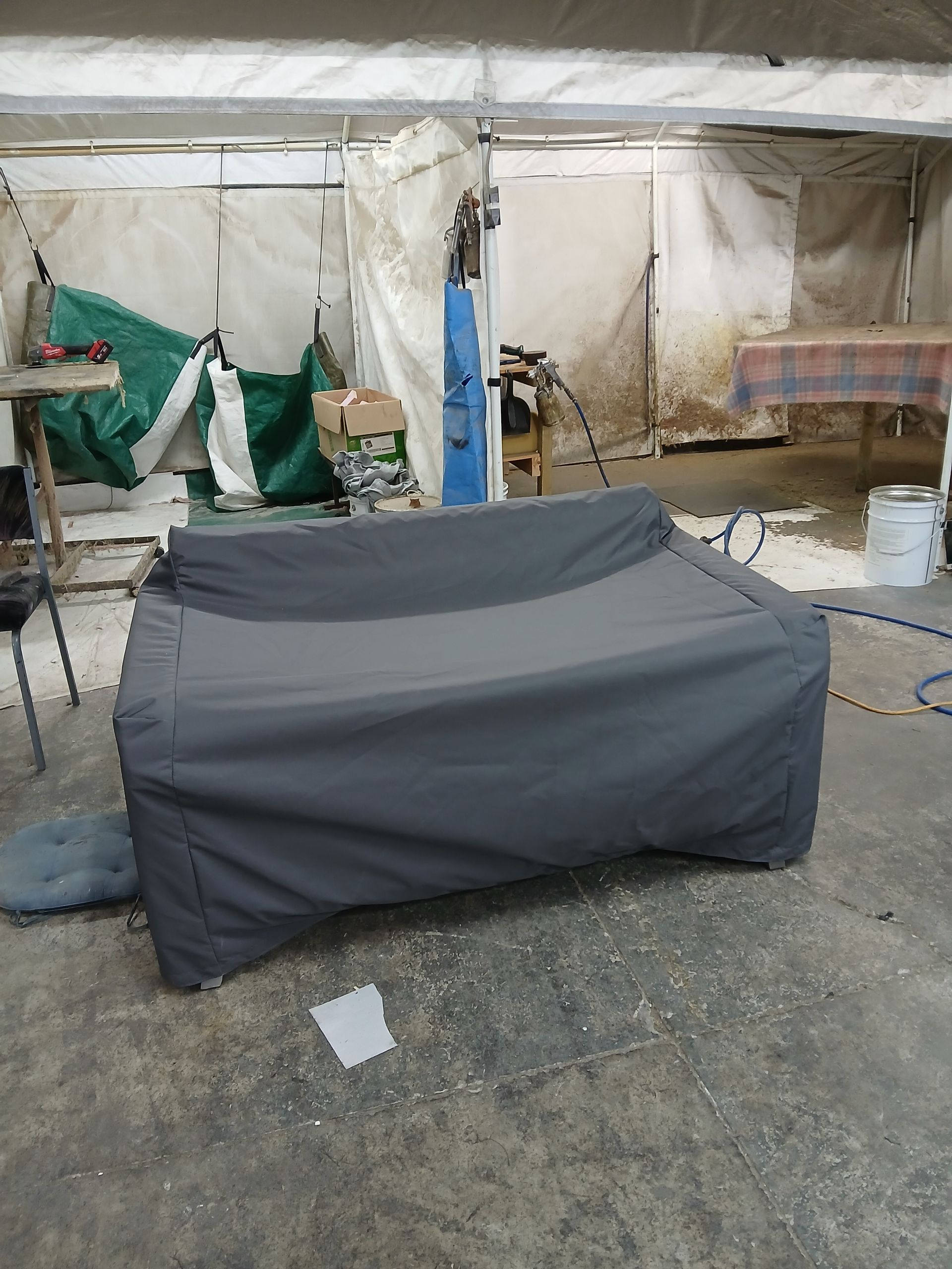 Gray couch covered with a tarp in a cluttered workshop.
