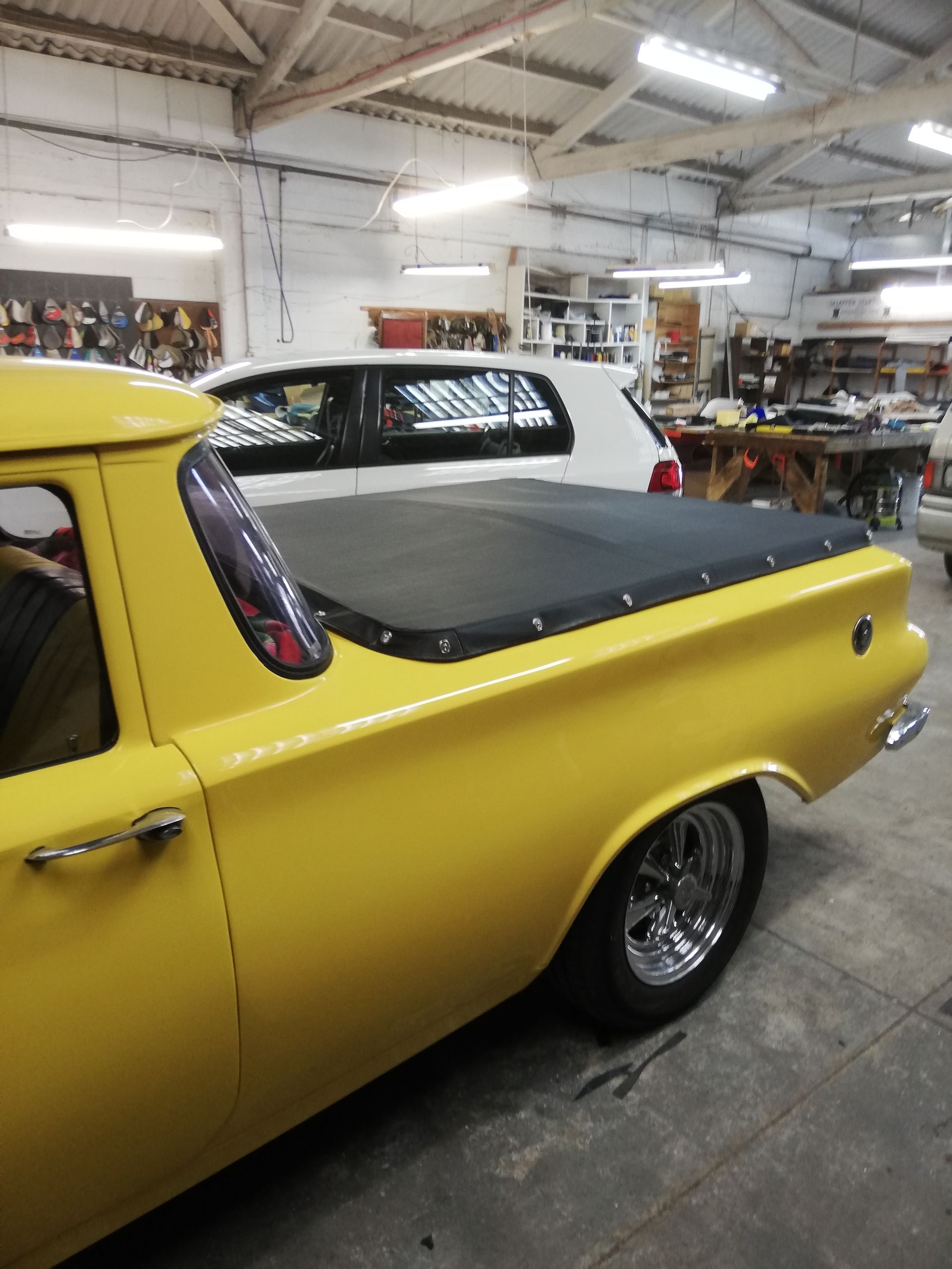 Yellow classic car with black bed cover parked in a garage.