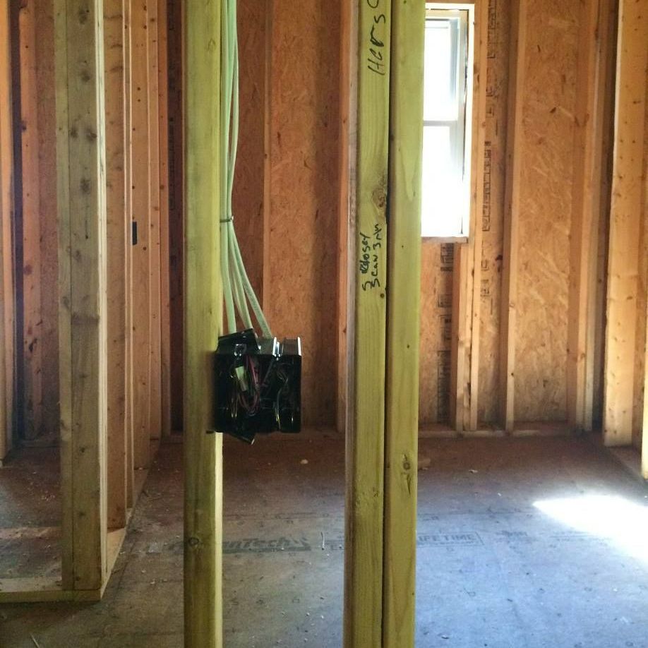 A room in a house under construction with a box of wires hanging from the ceiling