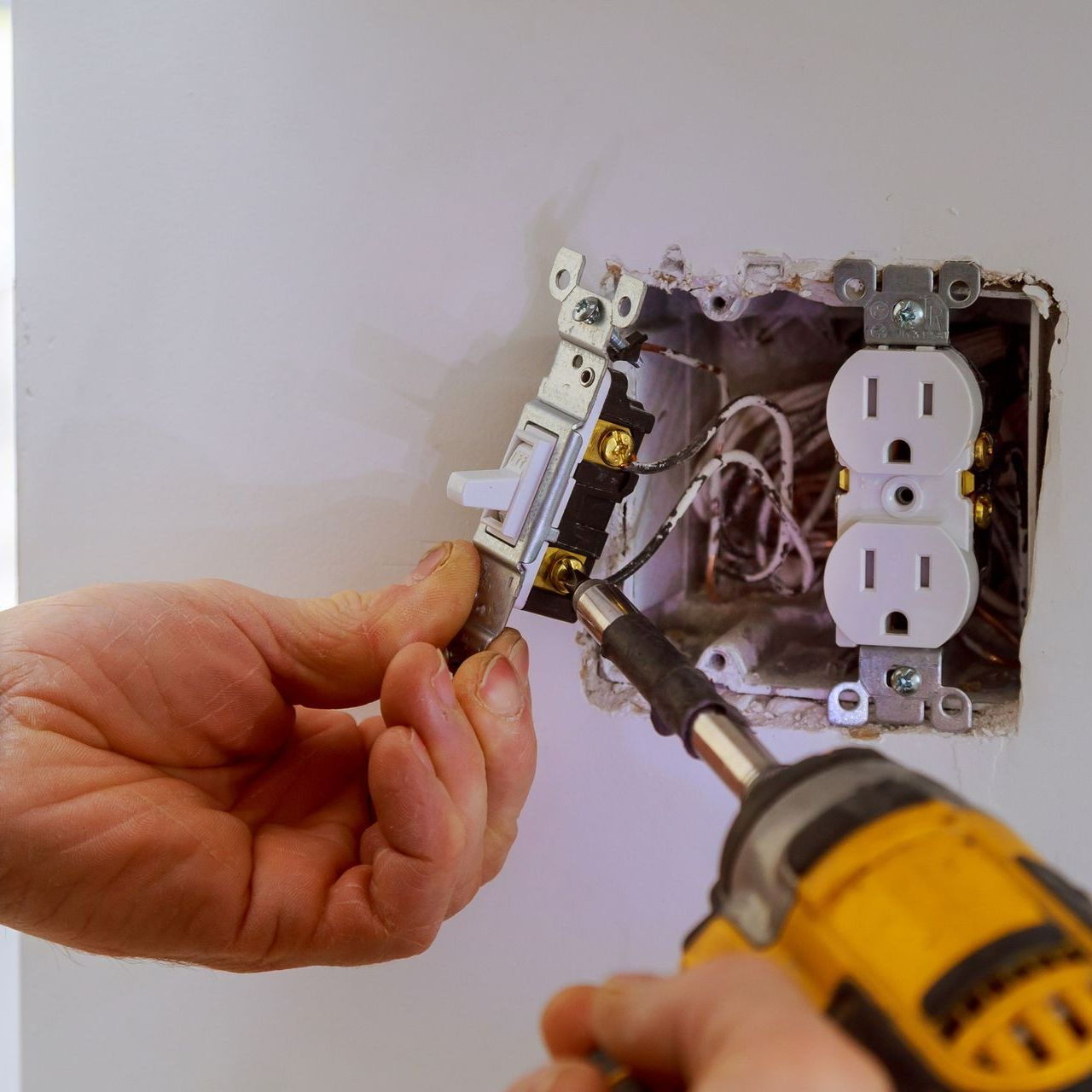 A person is working on an electrical outlet with a drill