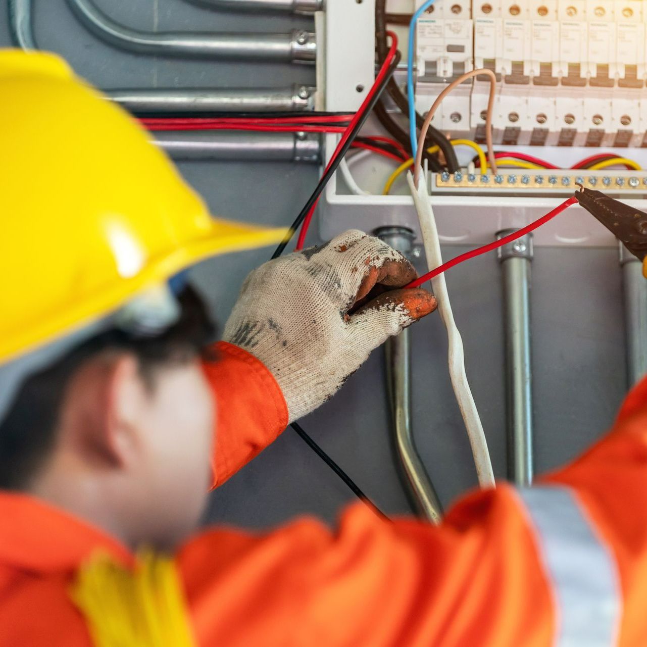 A man wearing a hard hat is working on an electrical box.