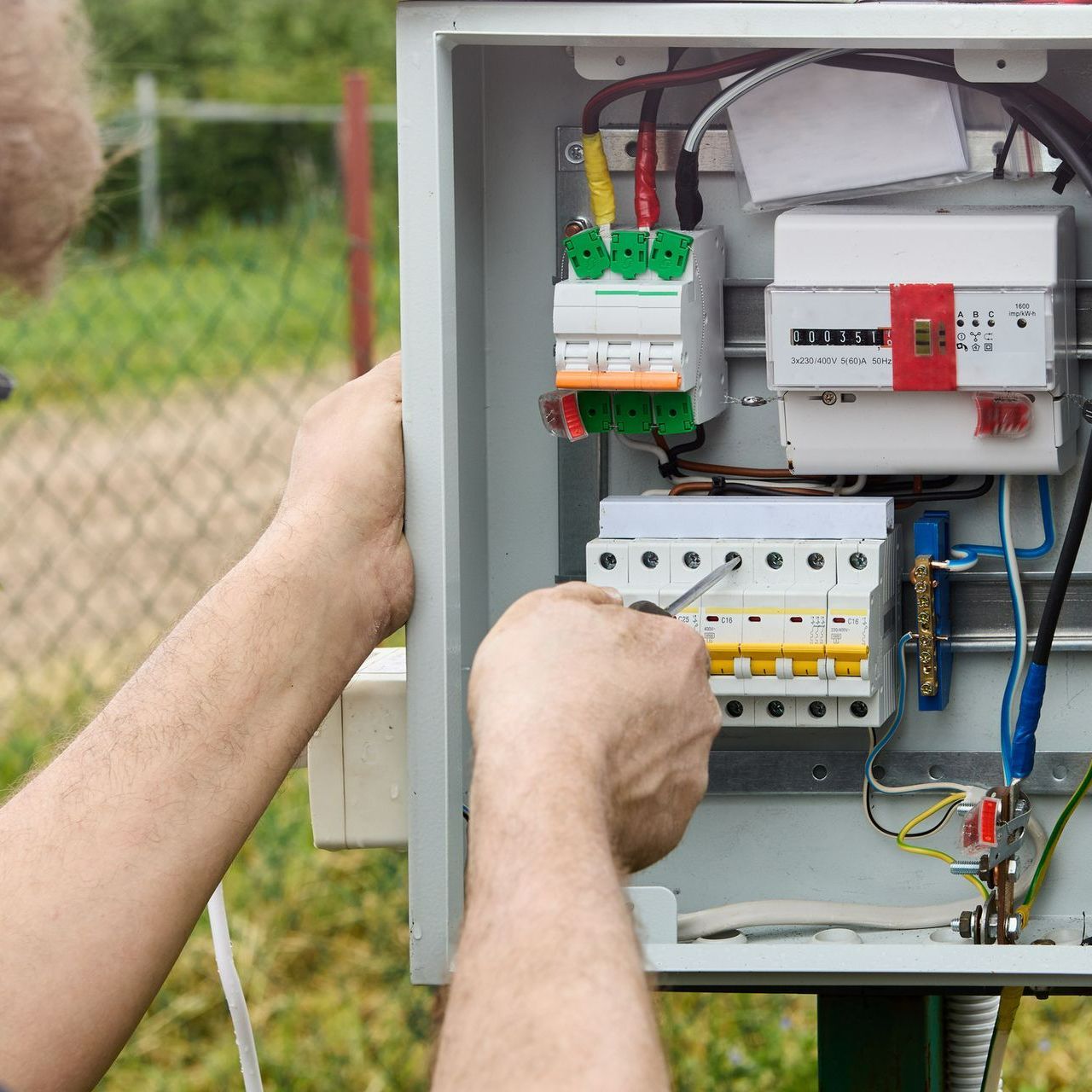 A man is working on an electrical box with a screwdriver