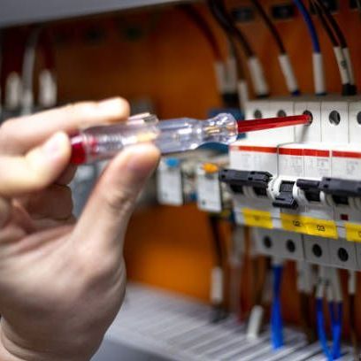 A person is holding a screwdriver in front of a circuit board.