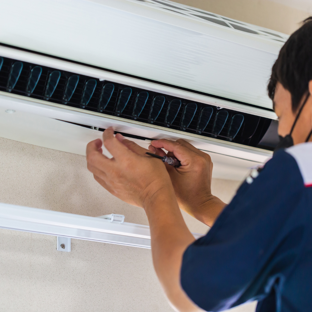 A technician uses a small tool to perform maintenance on an indoor wall-mounted air conditioning unit.