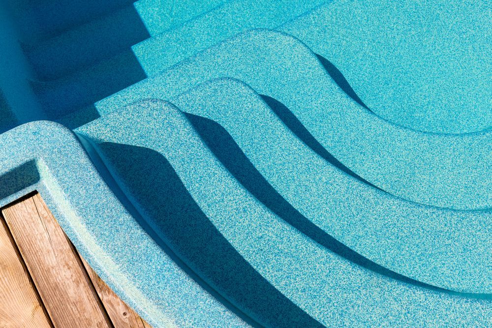 A close up of a swimming pool with stairs and a wooden deck.