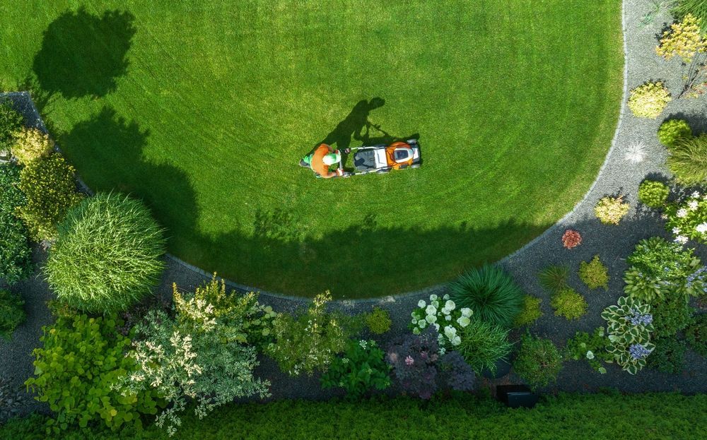 An aerial view of a person mowing a lush green lawn.