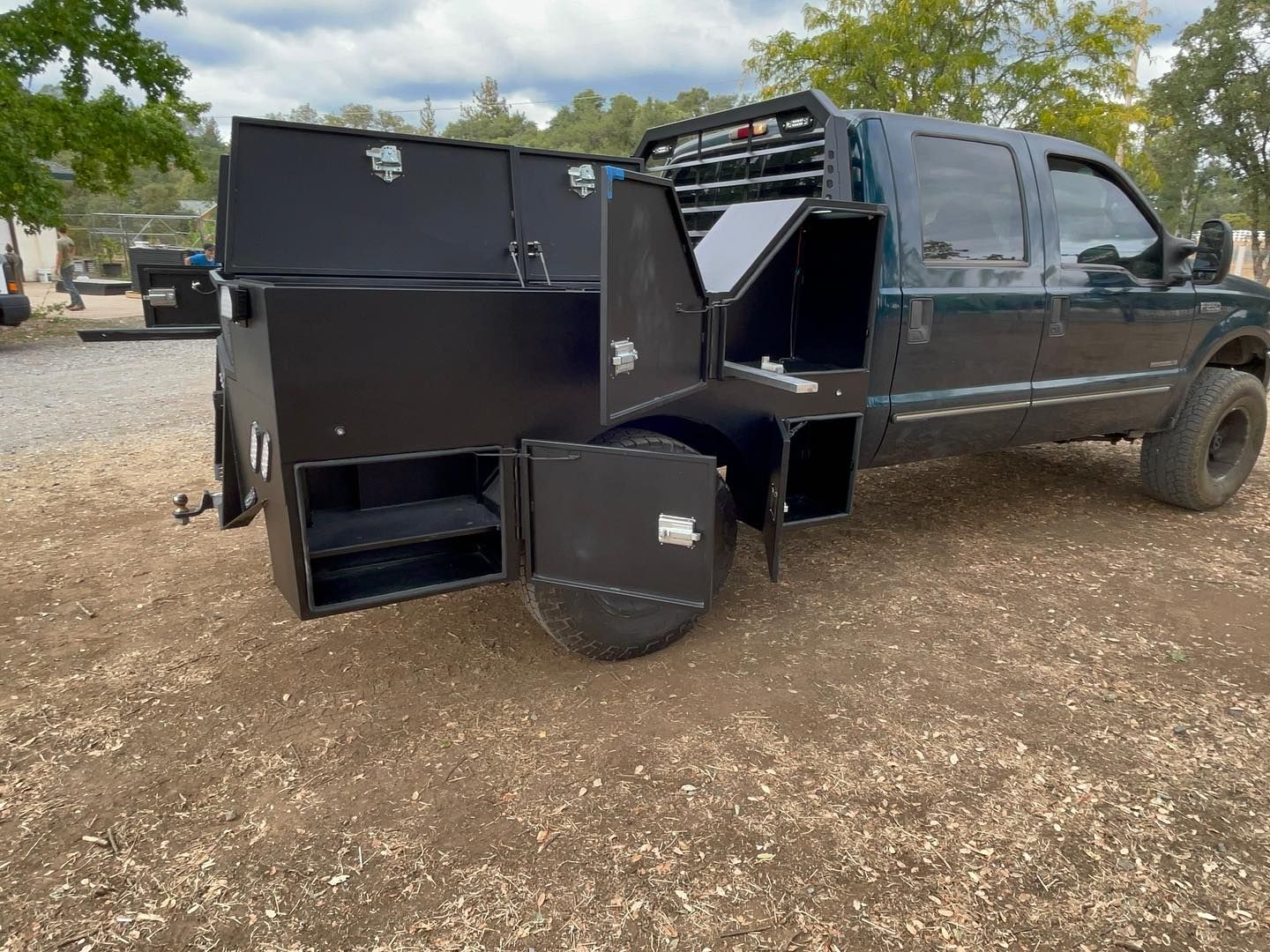 a black truck with a trailer attached to it is parked in a gravel lot .