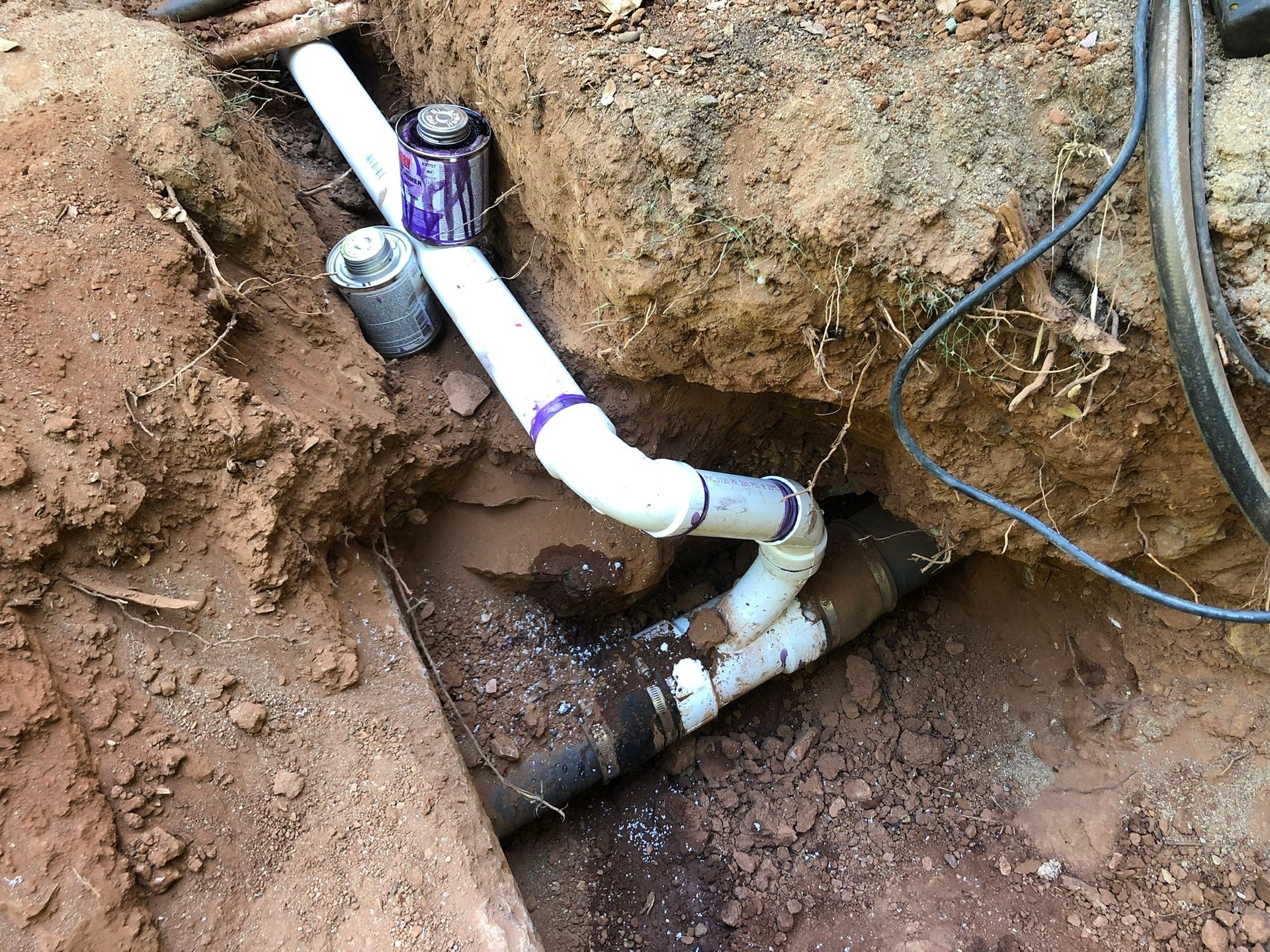 a white pipe is laying in the dirt next to a black pipe .