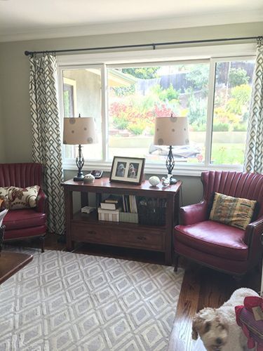 A living room with red chairs, a dog, a table and a window.