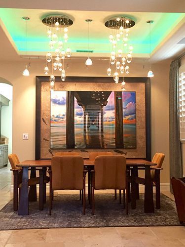 A dining room with a table and chairs and a painting on the wall.