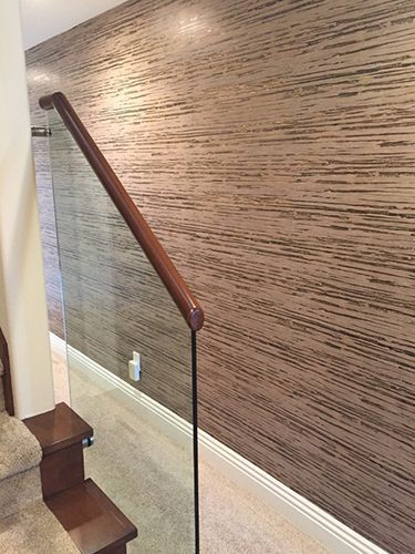 A staircase with a glass railing and a wall with wallpaper.