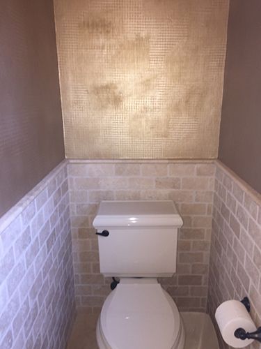 A toilet in a small bathroom with a brick wall behind it.