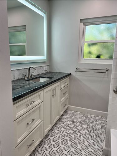 A bathroom with a sink , mirror and window.