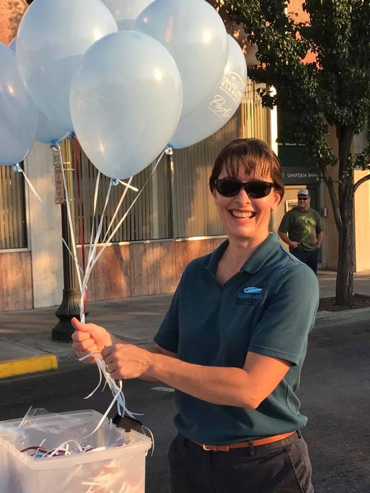 A woman is holding a bunch of blue balloons and smiling