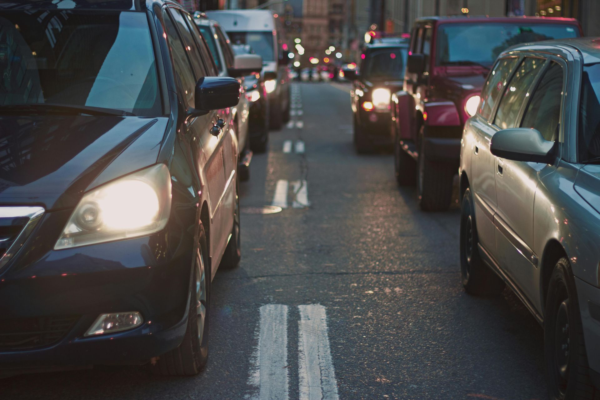 A row of cars are driving down a city street at night.