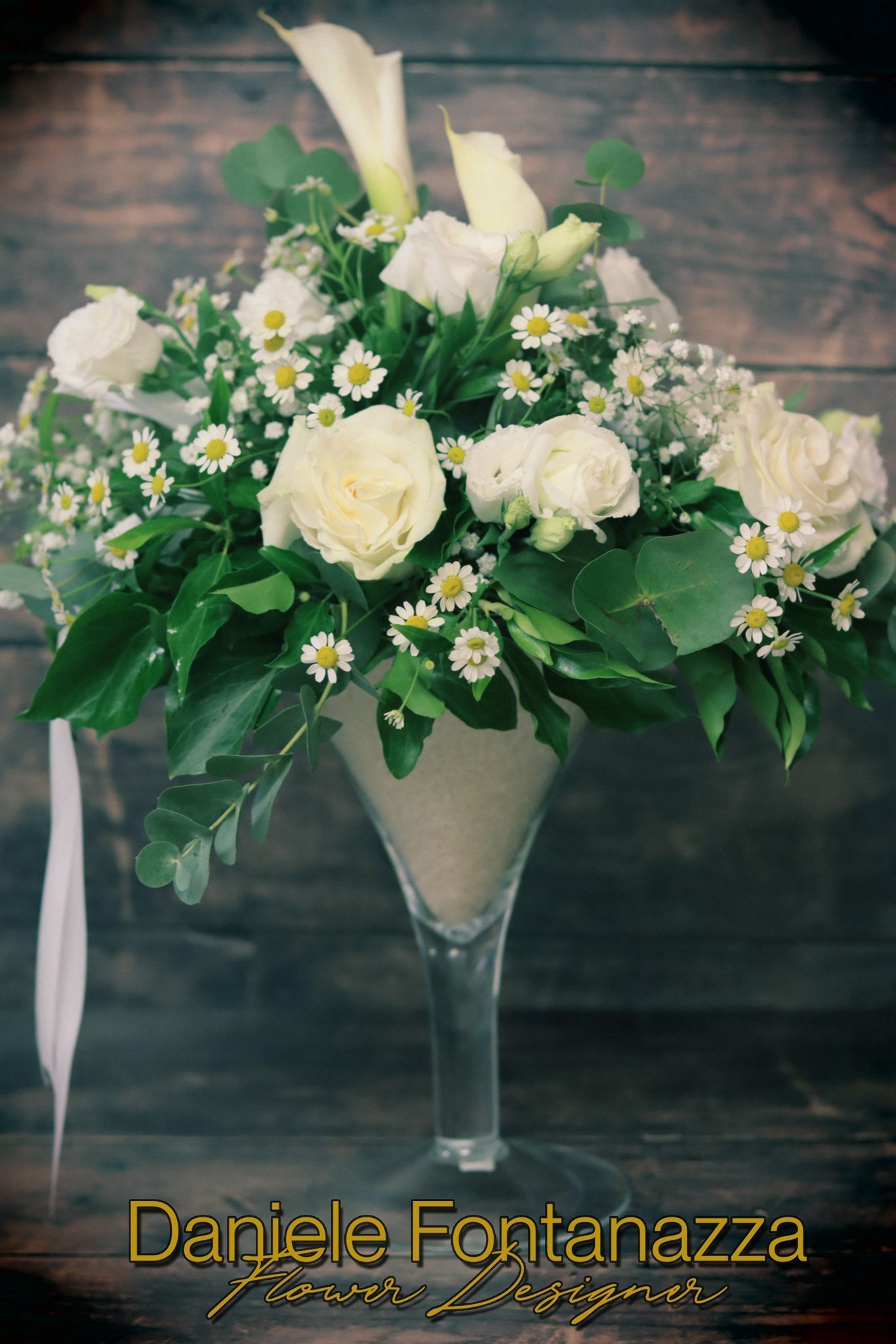 Fiori bianchi in un vaso di vetro da martini, su uno sfondo di legno.