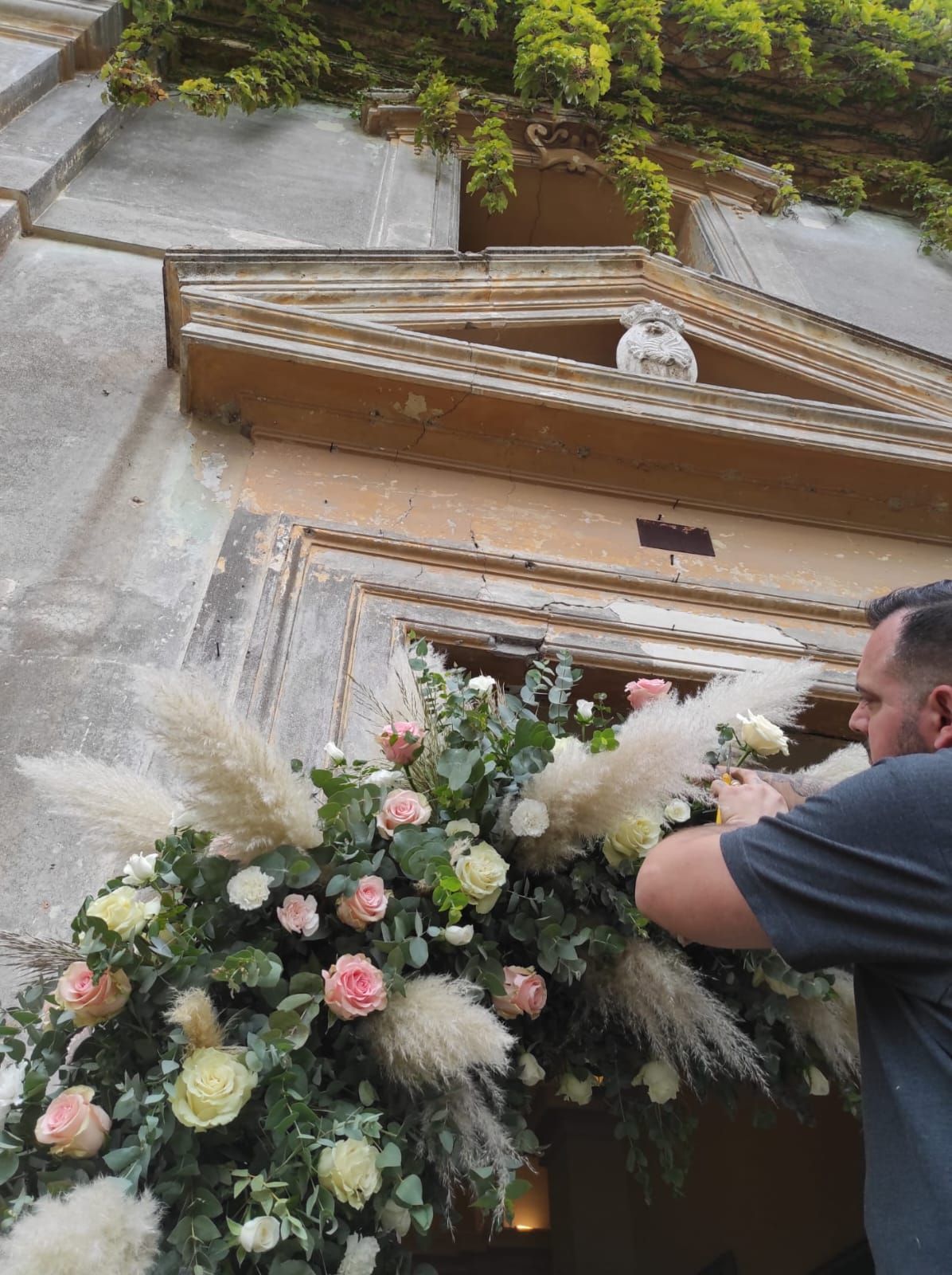 Uomo che sistema i fiori su una porta, con un arco floreale decorativo raffigurante erba della pampa e rose.