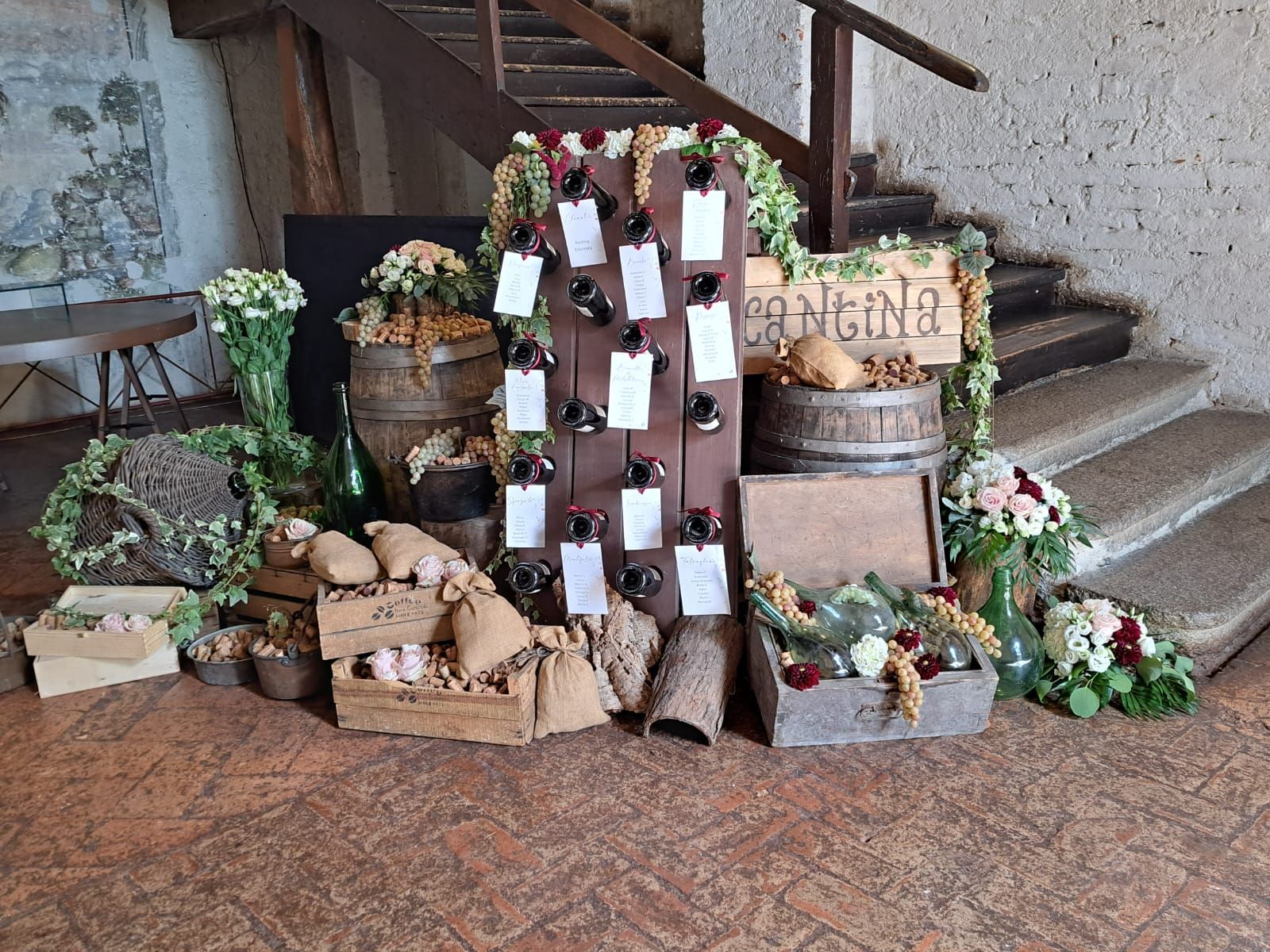 Espositore per la disposizione dei posti a sedere per matrimoni con botti di vino, fiori e cartellini scritti a mano.