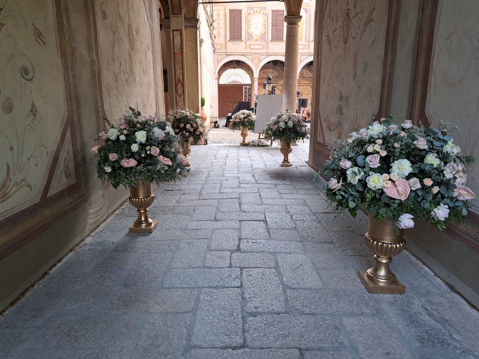 Composizioni floreali in urne dorate costeggiano un vialetto in pietra che conduce a un cortile ad arco.