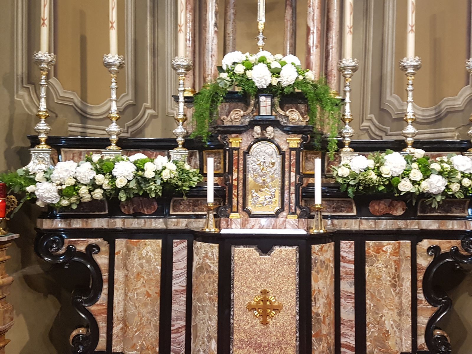 Altare con fiori bianchi, candele e intagli decorativi in una chiesa. Dettagli in marmo e oro.