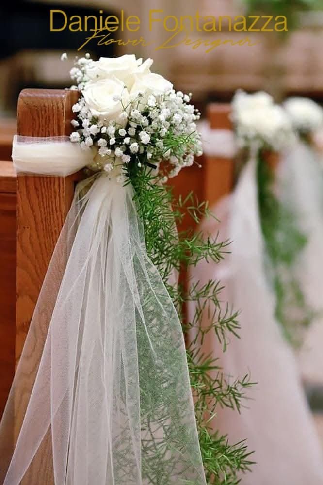 Composizioni floreali bianche con verde e tessuto trasparente decorano i banchi di legno di una chiesa.