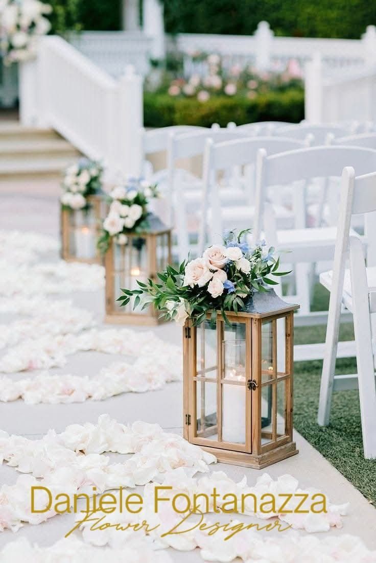 Navata centrale per matrimoni con lanterne, sedie bianche e petali di fiori.