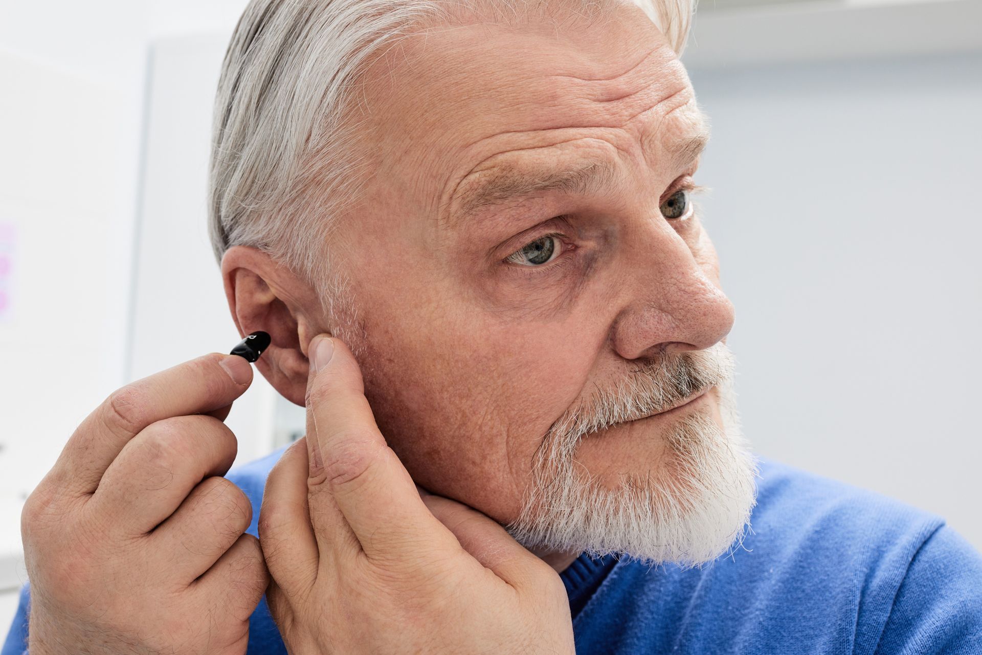 Grey-haired senior man with hearing impairment using hearing aid.