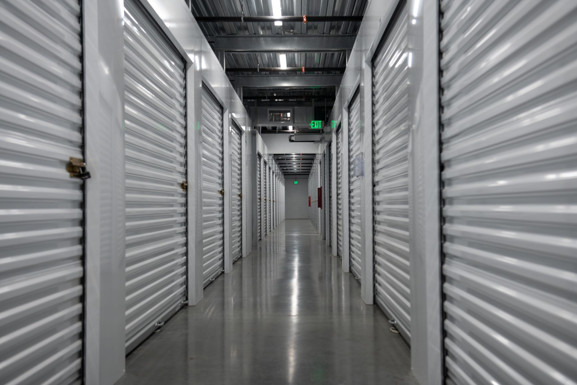 An empty indoor storage facility hallway lined with closed metal roll-up doors on both sides