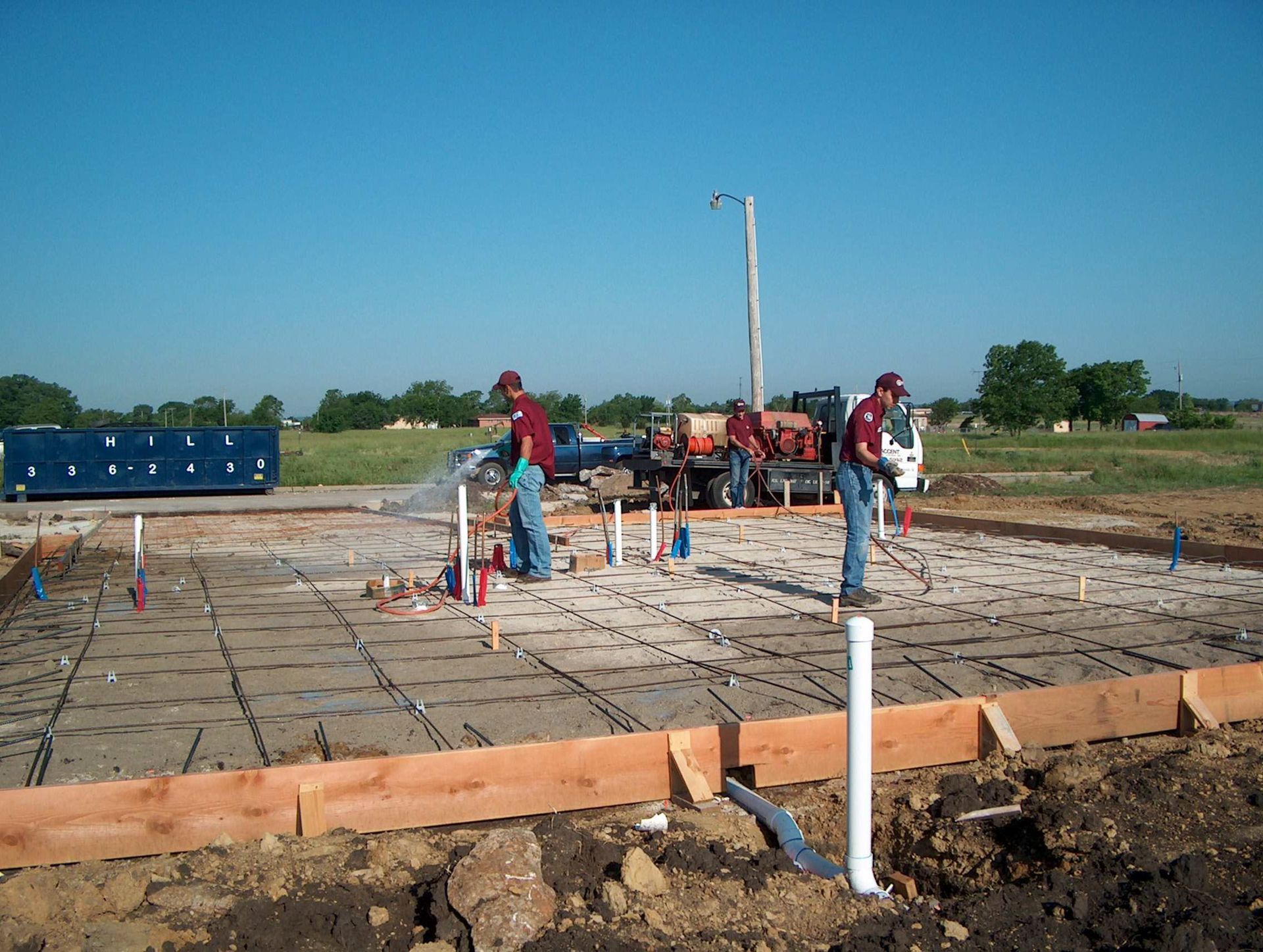 Workers at a construction site pouring concrete and laying foundations under a clear blue sky