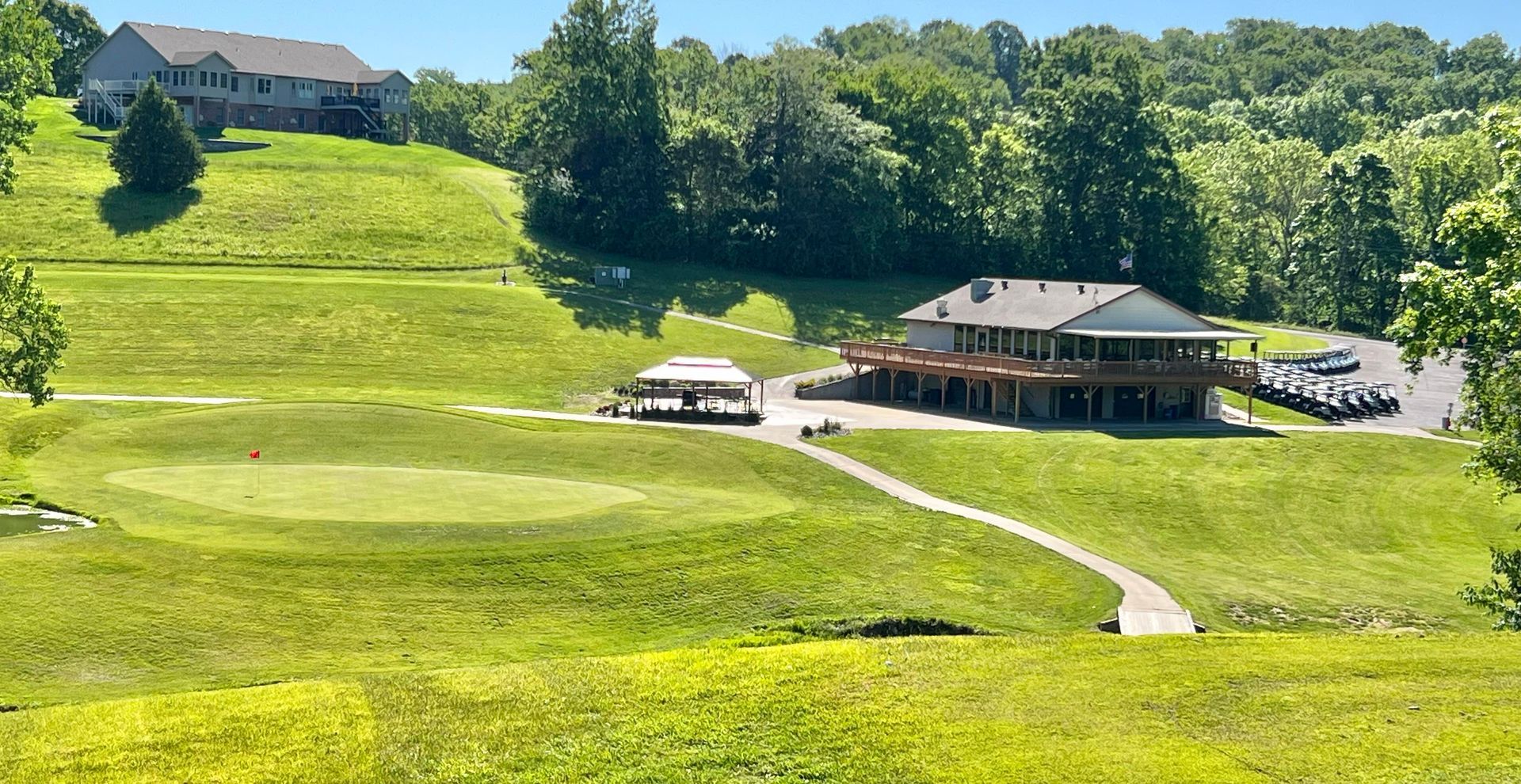 Sunny green hillside with houses, a winding path, and trees in the background
