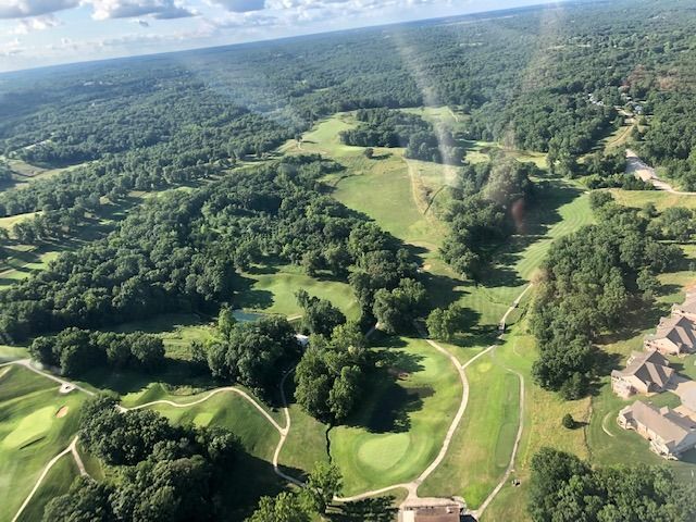 Aerial view of a lush green golf course with winding fairways and surrounding trees.