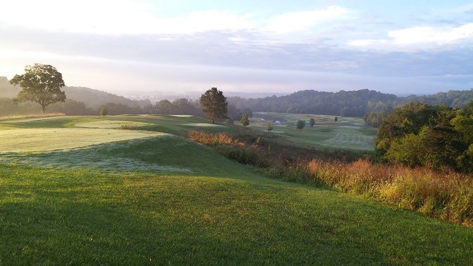 Sunlit green hillside with trees, frosty fields, and distant rolling hills at dawn