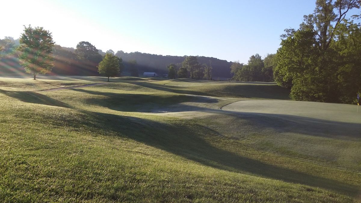 Sunlit golf course with green fairways, trees, and long morning shadows
