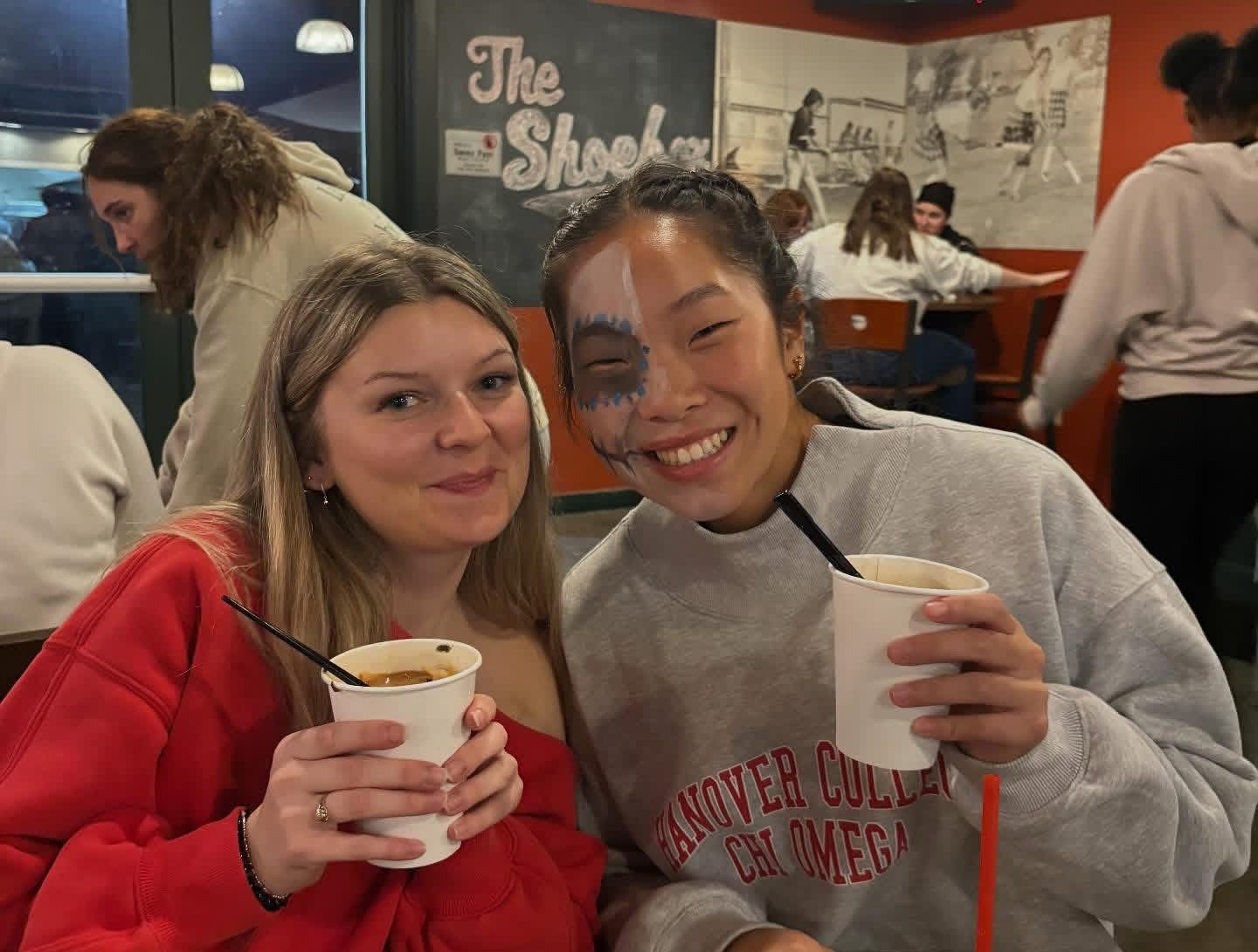 Two smiling people holding desserts, indoors. One wears a hoodie, the other a sweater.