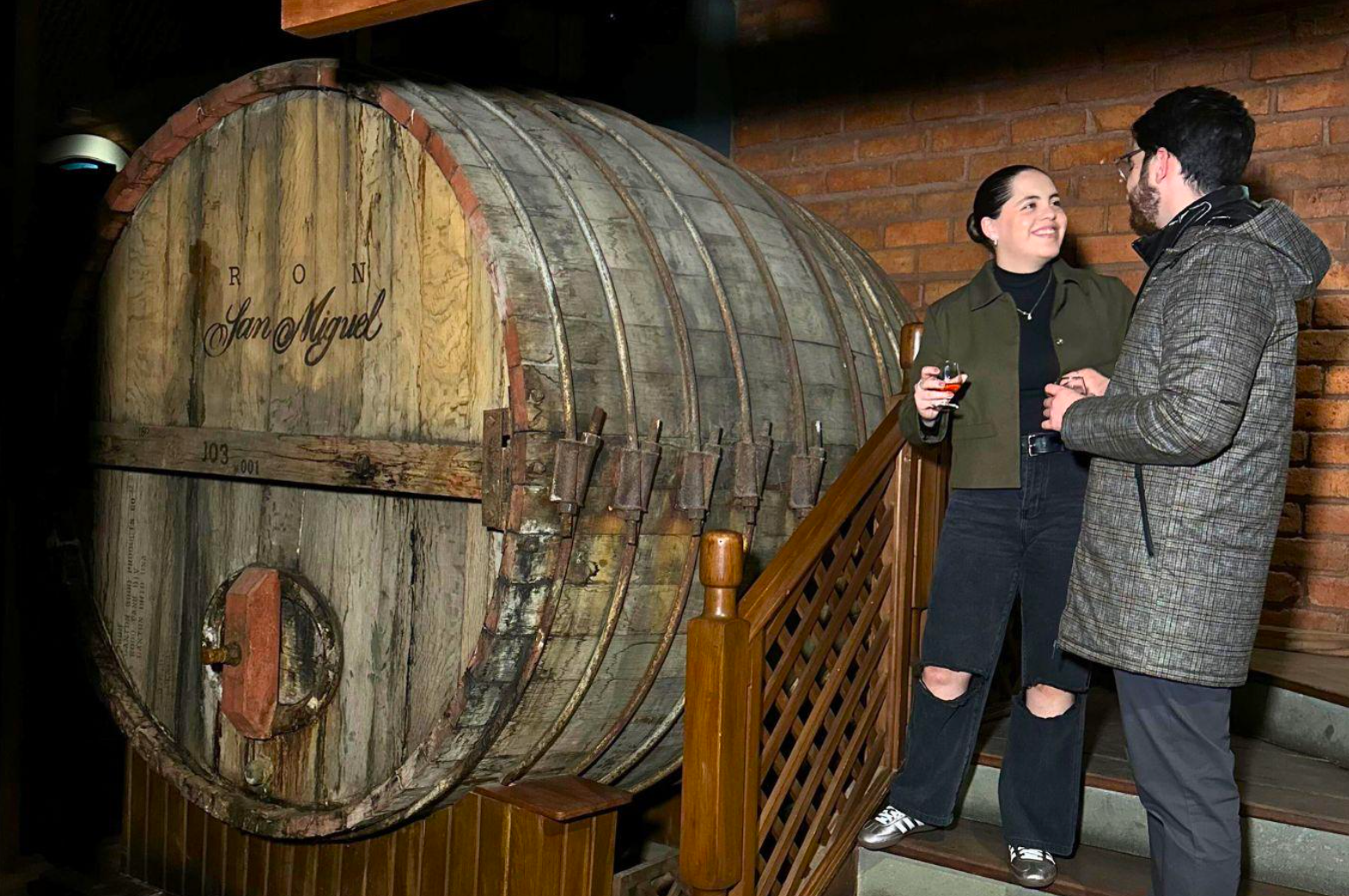 A man and a woman are standing next to a large wooden barrel.