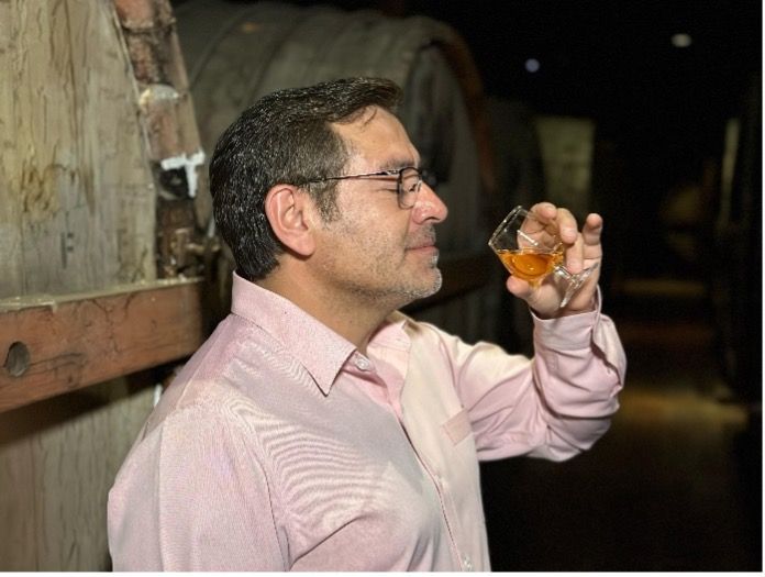 A man in a pink shirt is smelling a glass of Ron San Miguel