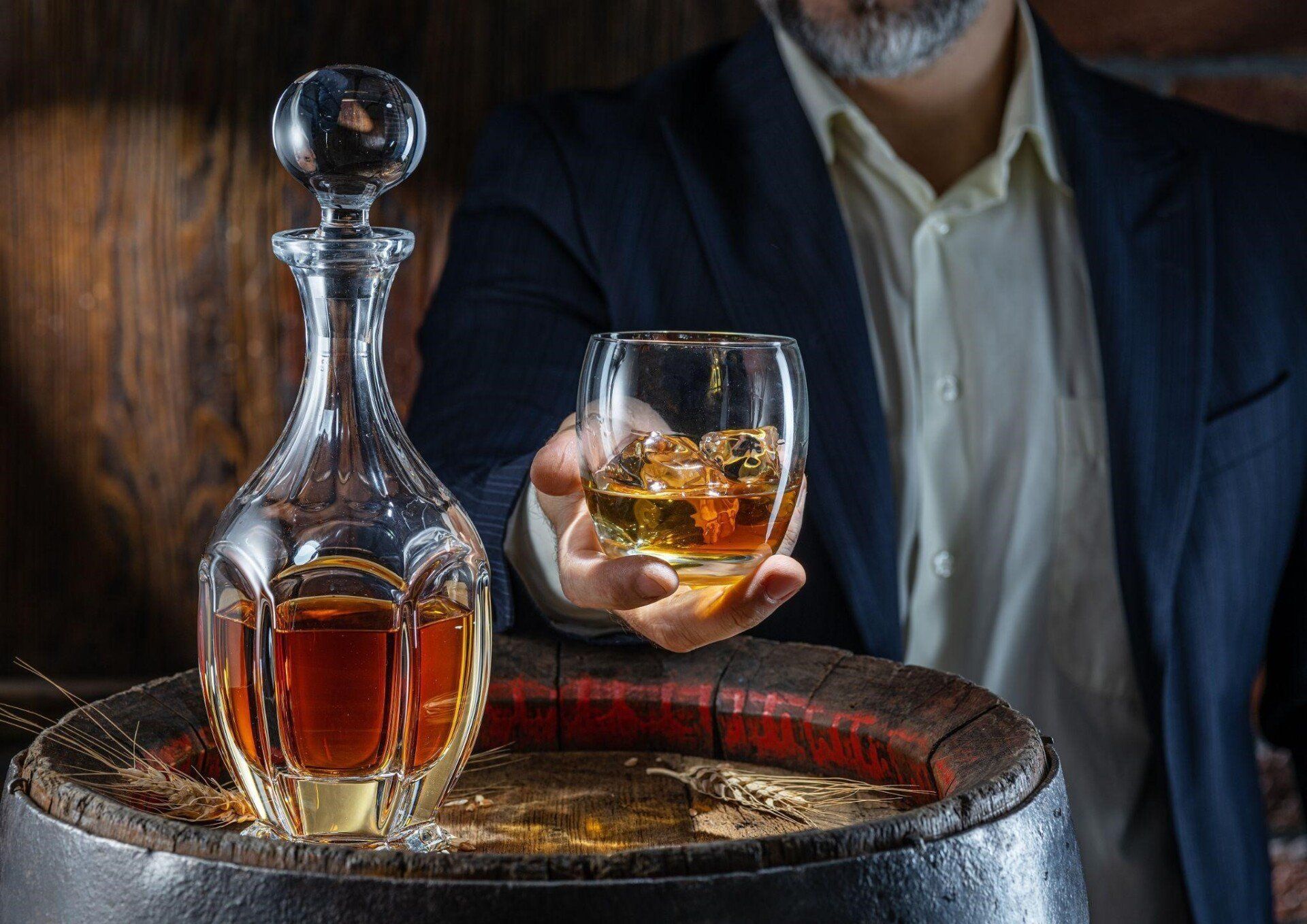 Hombre degustando un vaso de ron sobre barrica de madera