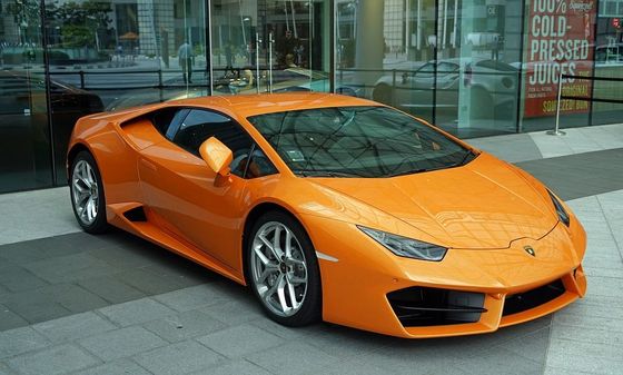 An orange sports car is parked in front of a store that sells cold pressed juices
