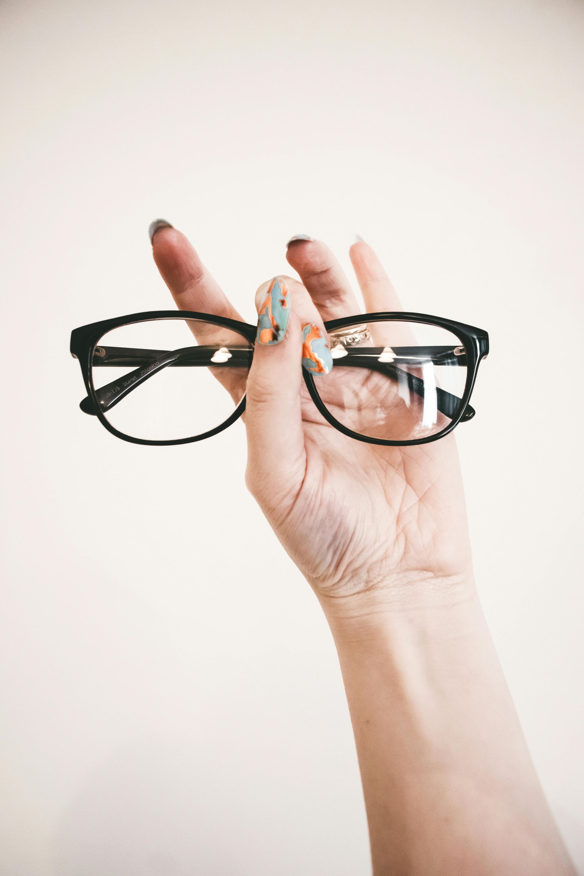 Hand holding black-framed glasses with clear lenses against a white background.