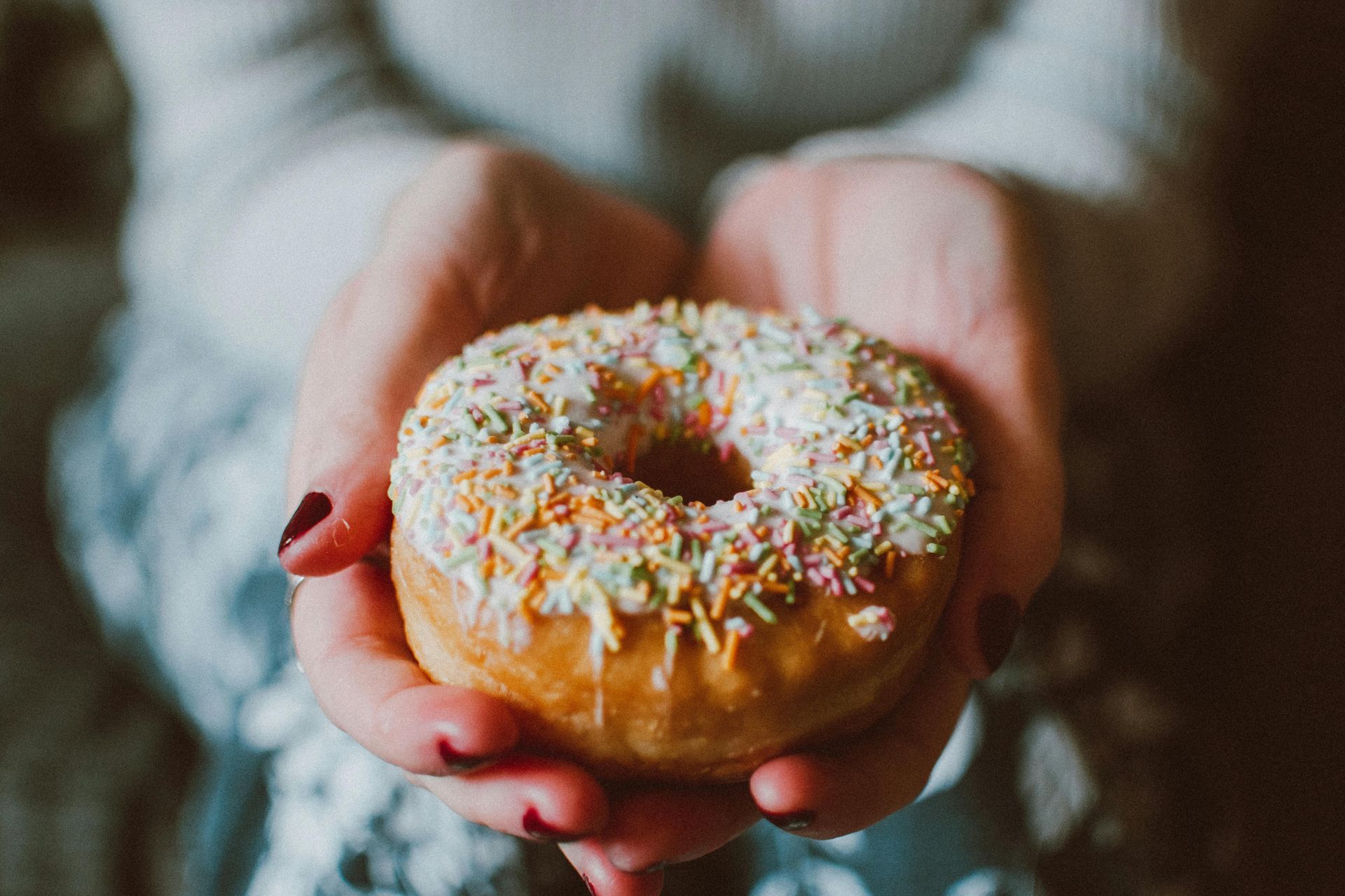 Person holding a glazed donut with colorful sprinkles.