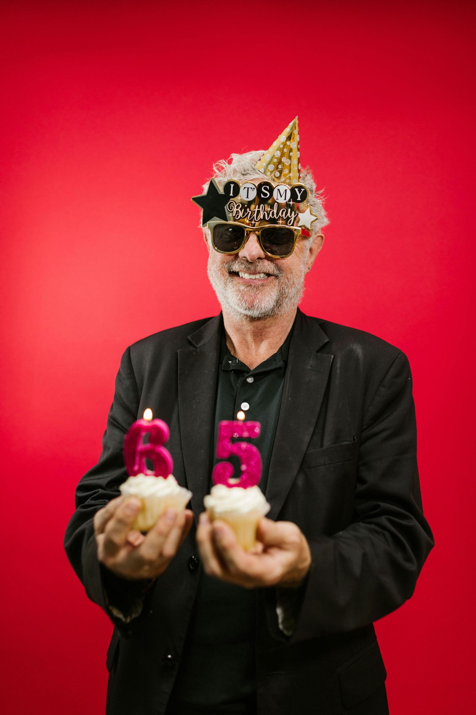 Man with party hat and sunglasses holds cupcakes with 