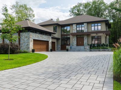 Modern two-story house with stone facade, large windows, and gray brick driveway.