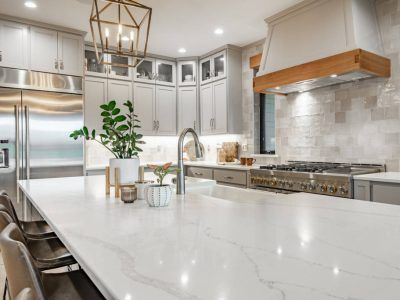 Modern kitchen with white countertops, gray cabinets, stainless steel appliances, and a wooden range hood.
