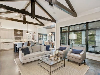 Open-concept living space with dark ceiling beams, light gray walls, and large windows overlooking a patio.
