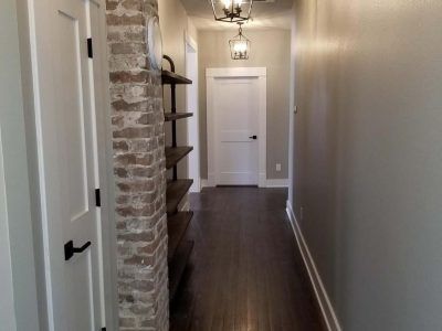 Narrow hallway with dark wood floor, white doors, and exposed brick column.