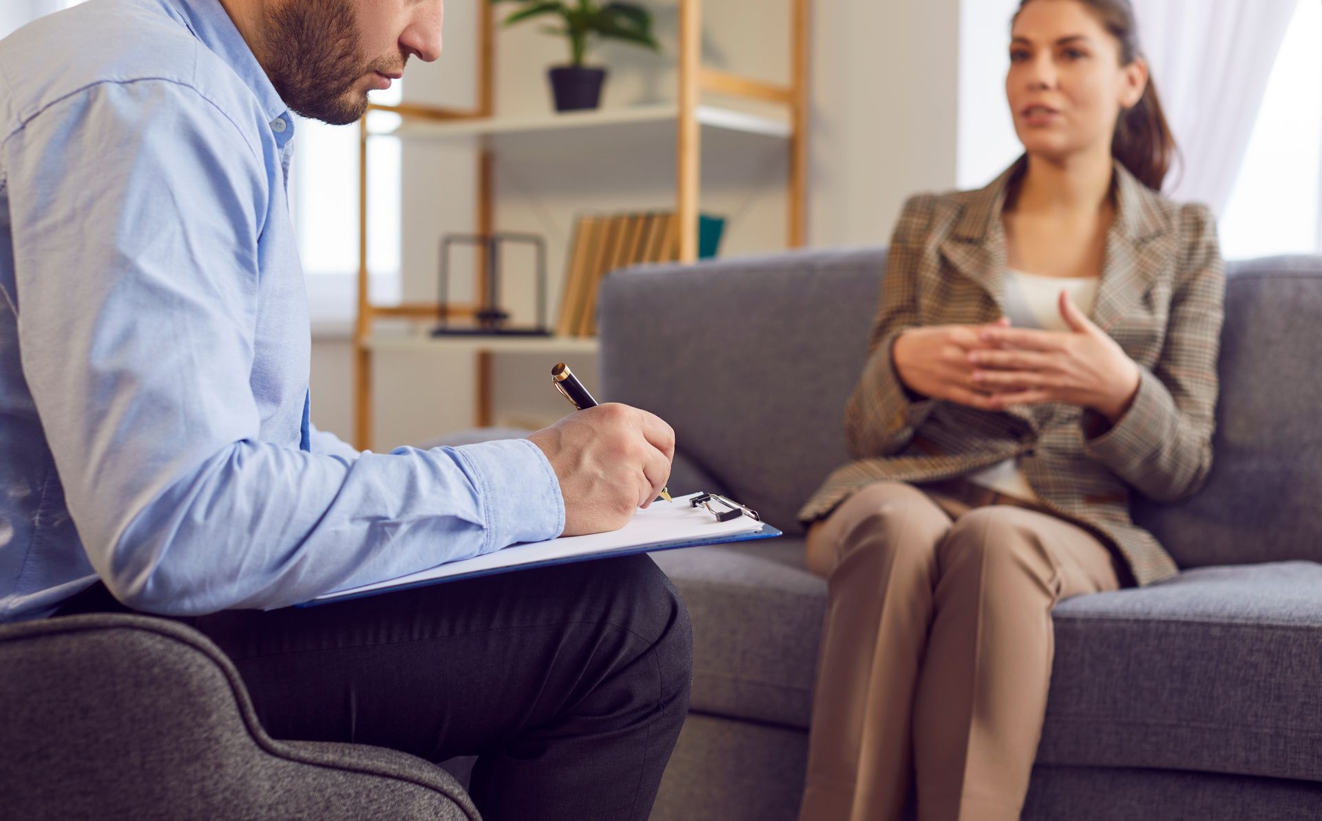 Therapist taking notes while a woman speaks on a sofa in a counseling office
