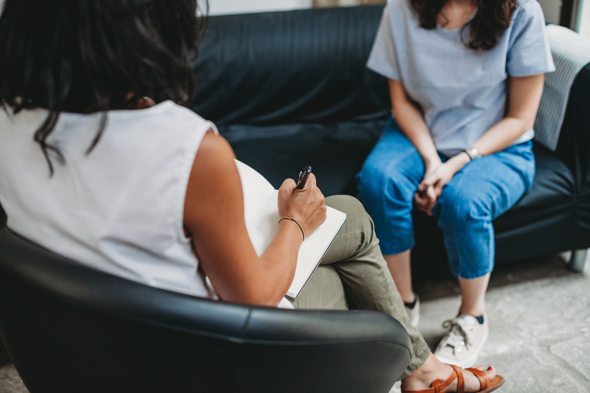 Two people sit facing each other on a couch during a conversation in a living room.