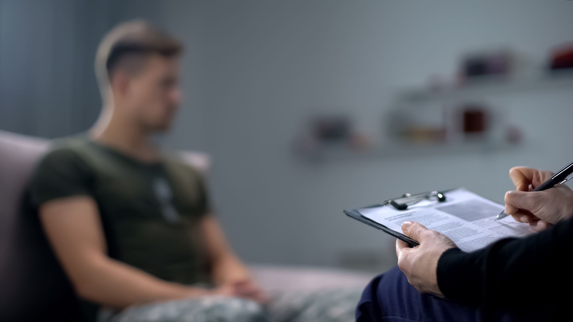 Therapist taking notes while meeting with a blurred seated client in a counseling office